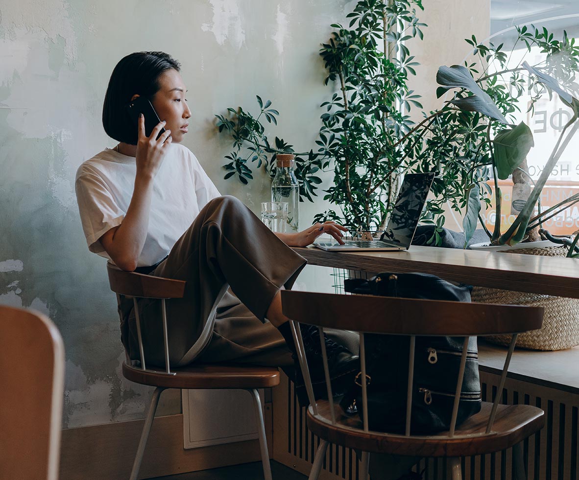 Person seated at desk with laptop computer in front of large window with plants.